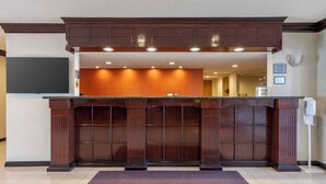 A reception desk with a dark wood finish, a flat-screen TV mounted above it, and a sign indicating check-in/out procedures.