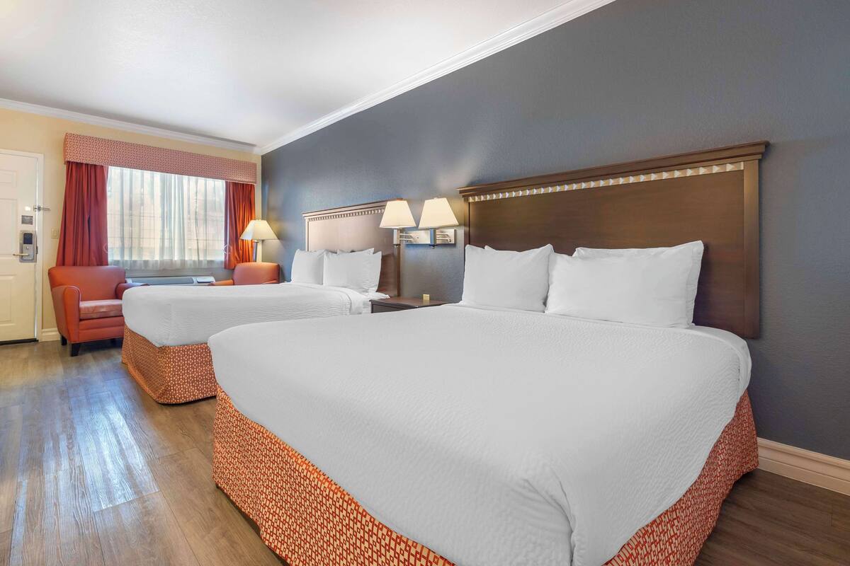 Quarto de hotel com duas camas, uma escrivaninha, uma cadeira e uma janela com cortinas.