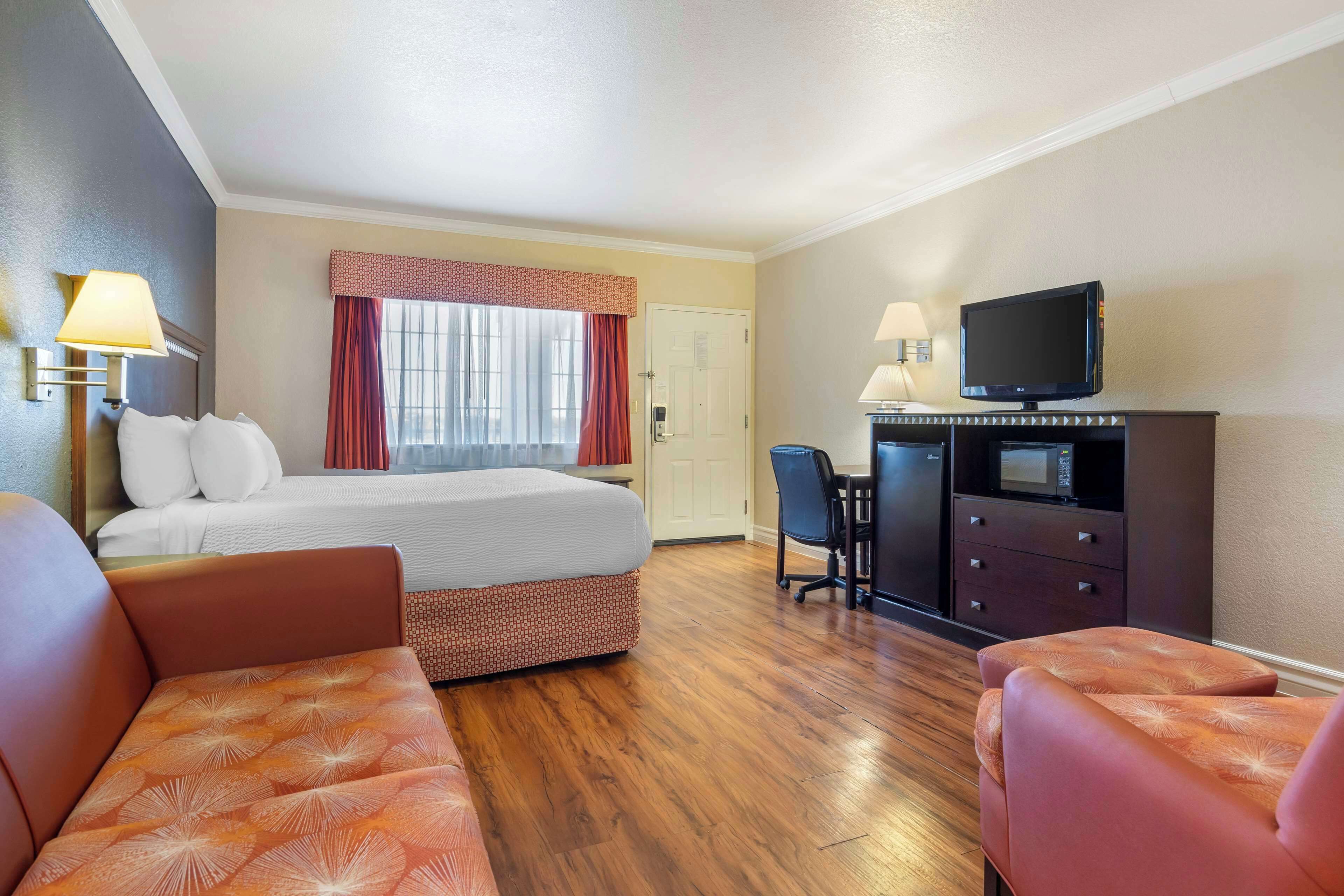 A hotel room with a bed, two armchairs, a desk with a chair, a television, and a microwave.