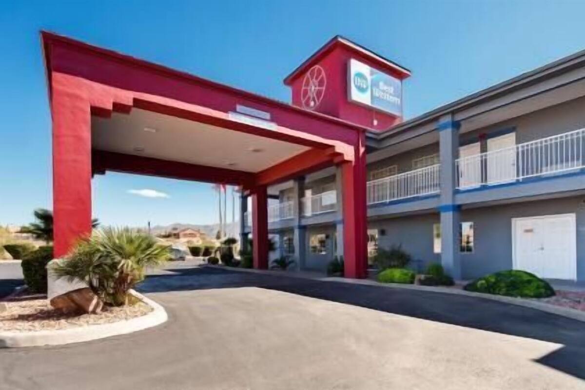 Um motel de vários andares com toldo vermelho, placa de posto de gasolina e fachada azul e branca.
