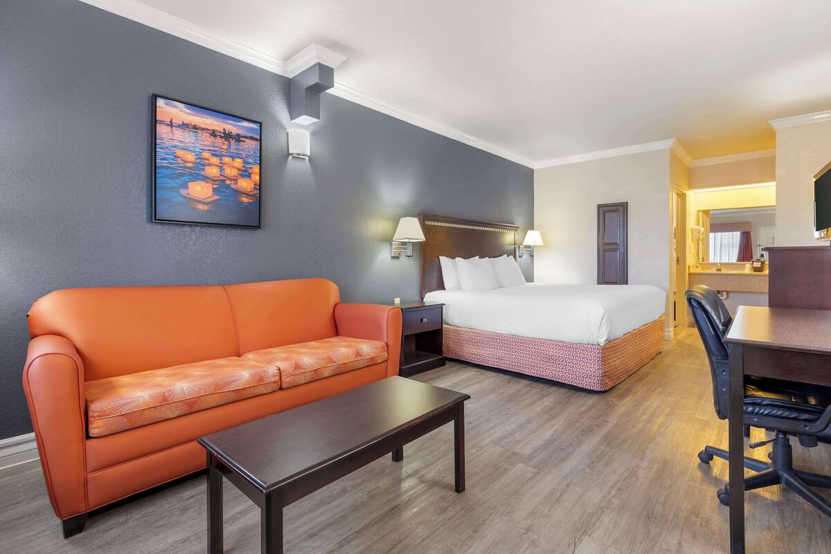 Quarto de hotel com cama, sofá, escrivaninha e mesa de cabeceira.