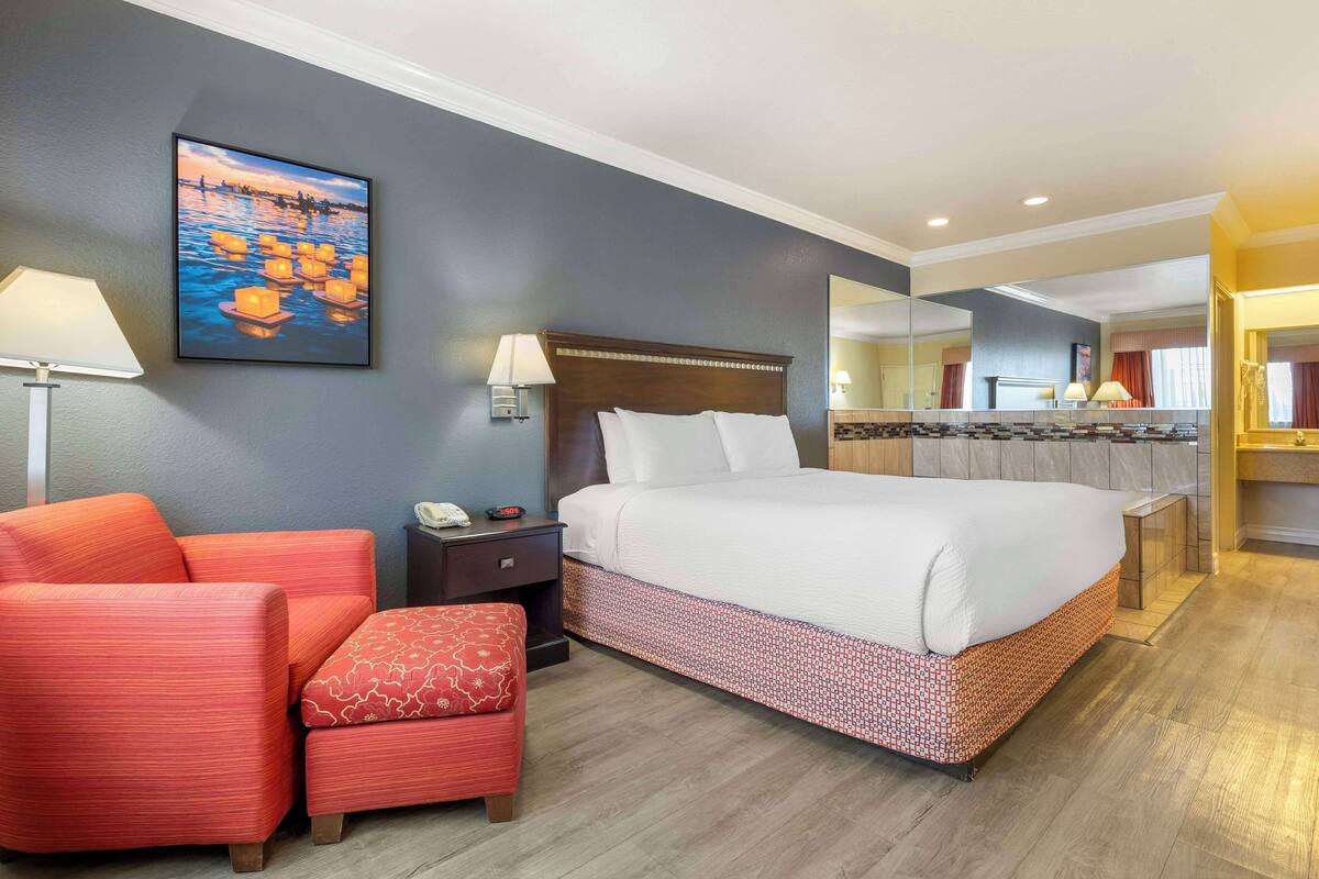 Quarto de hotel com cama, poltrona, mesa de cabeceira, luminária e um quadro na parede.