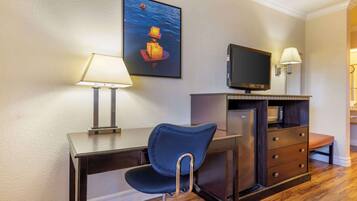 A hotel room with a desk, chair, TV, lamp, and a small refrigerator.