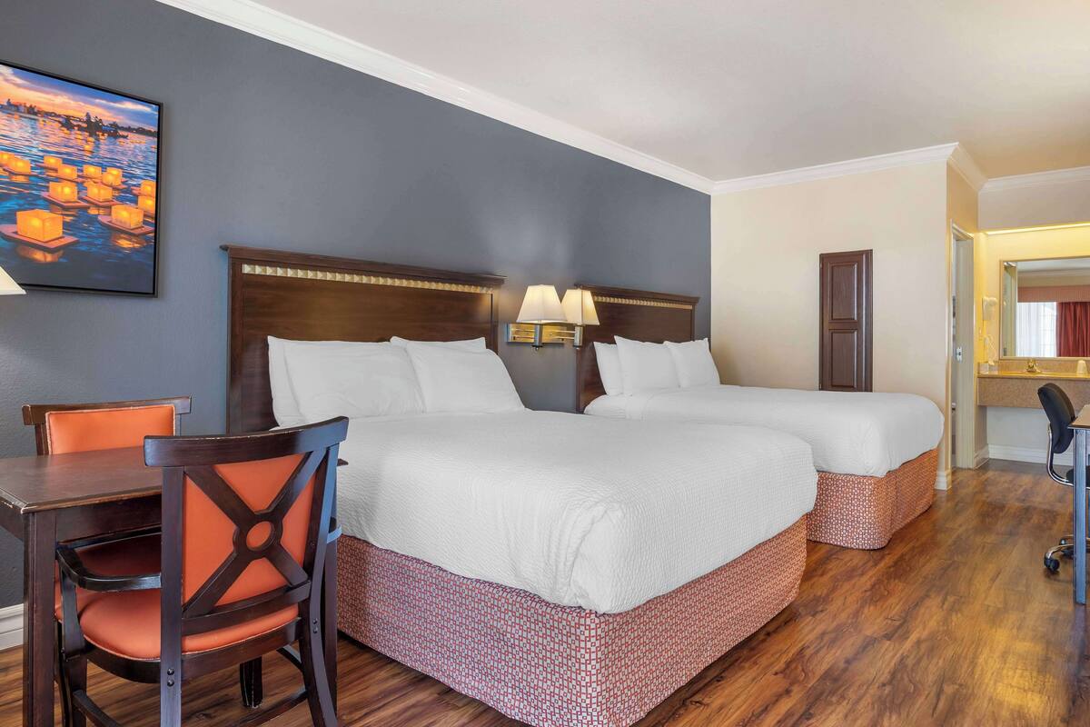 Quarto de hotel com duas camas, uma escrivaninha, uma cadeira e um quadro na parede.