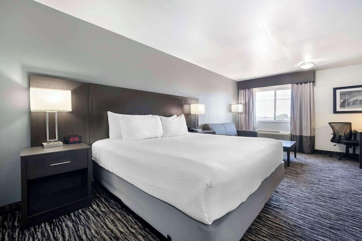 A hotel room with a large bed, bedside lamps, a desk, and a chair.