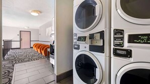 A laundry area with multiple washing machines, a patterned carpet, and a door leading to another room. - Best Western Santa Fe (Amarillo)