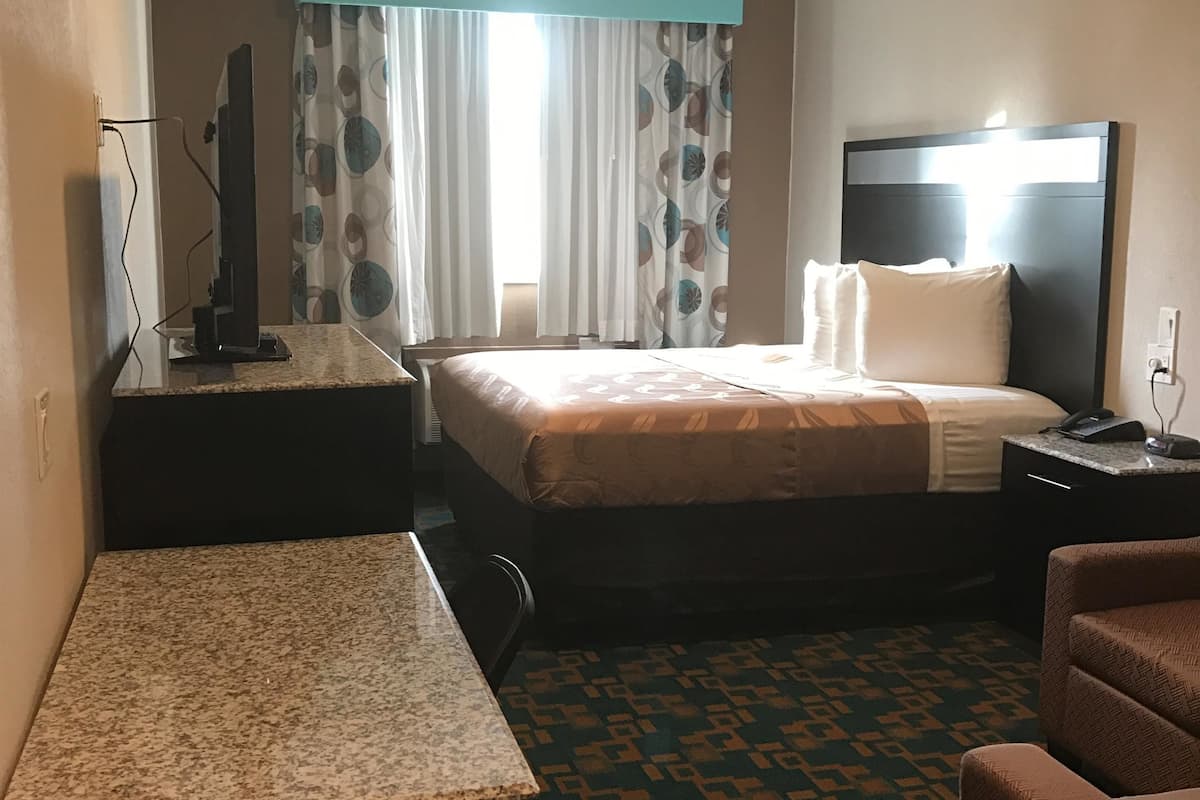 A hotel room with a bed, a desk, a chair, a television, and a nightstand.