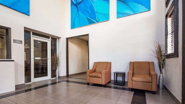 Un vestíbulo con dos sillones, un jarrón con plantas secas y una gran obra de arte azul en la pared.