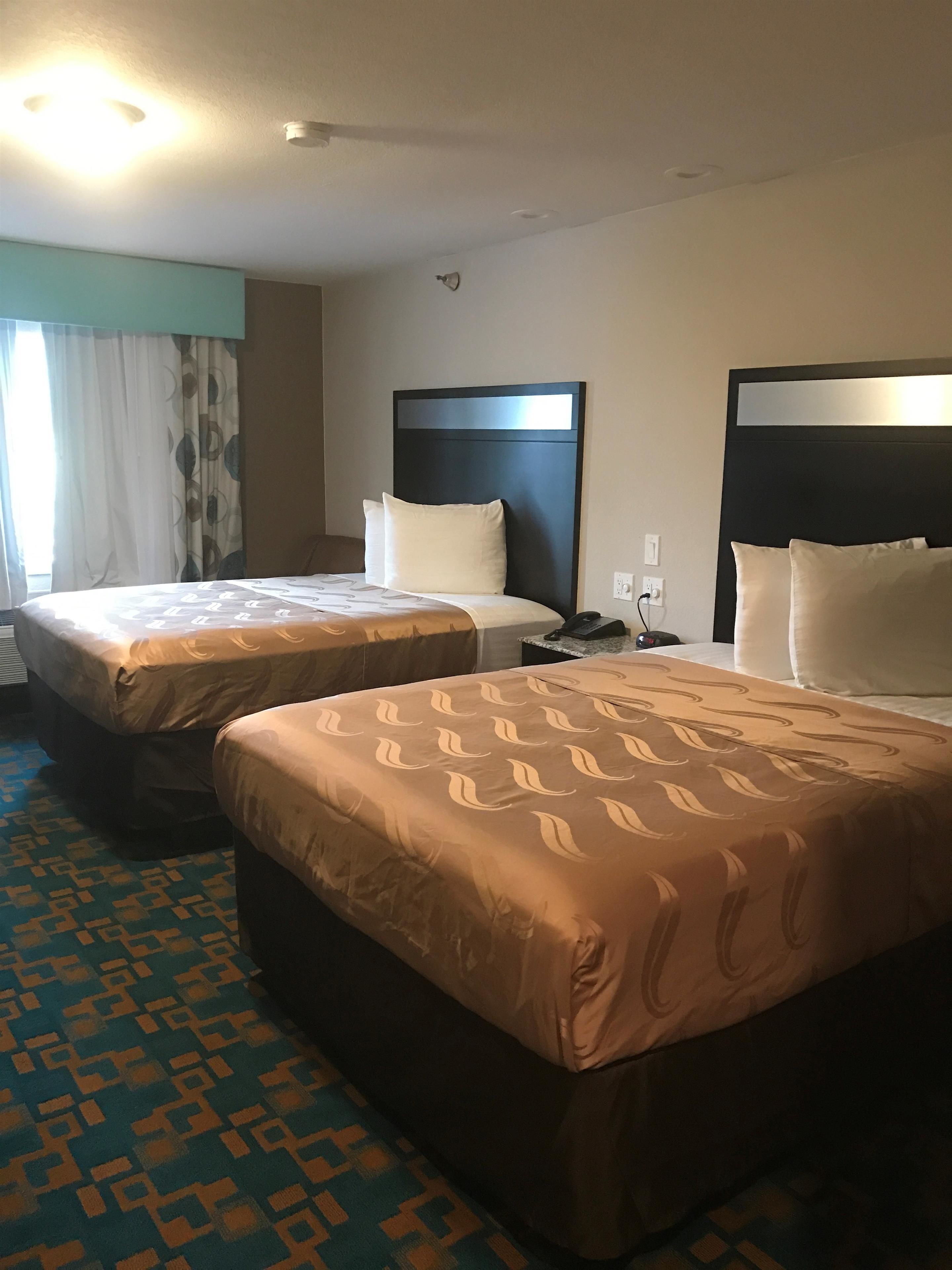 A hotel room with two beds, a patterned carpet, and a modern headboard design.