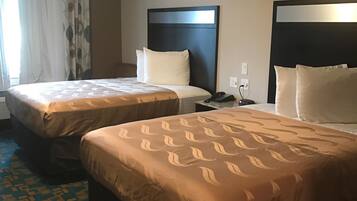 Hotellihuone, jossa on kaksi sänkyä, kuviollinen matto ja moderni sängynpääty.