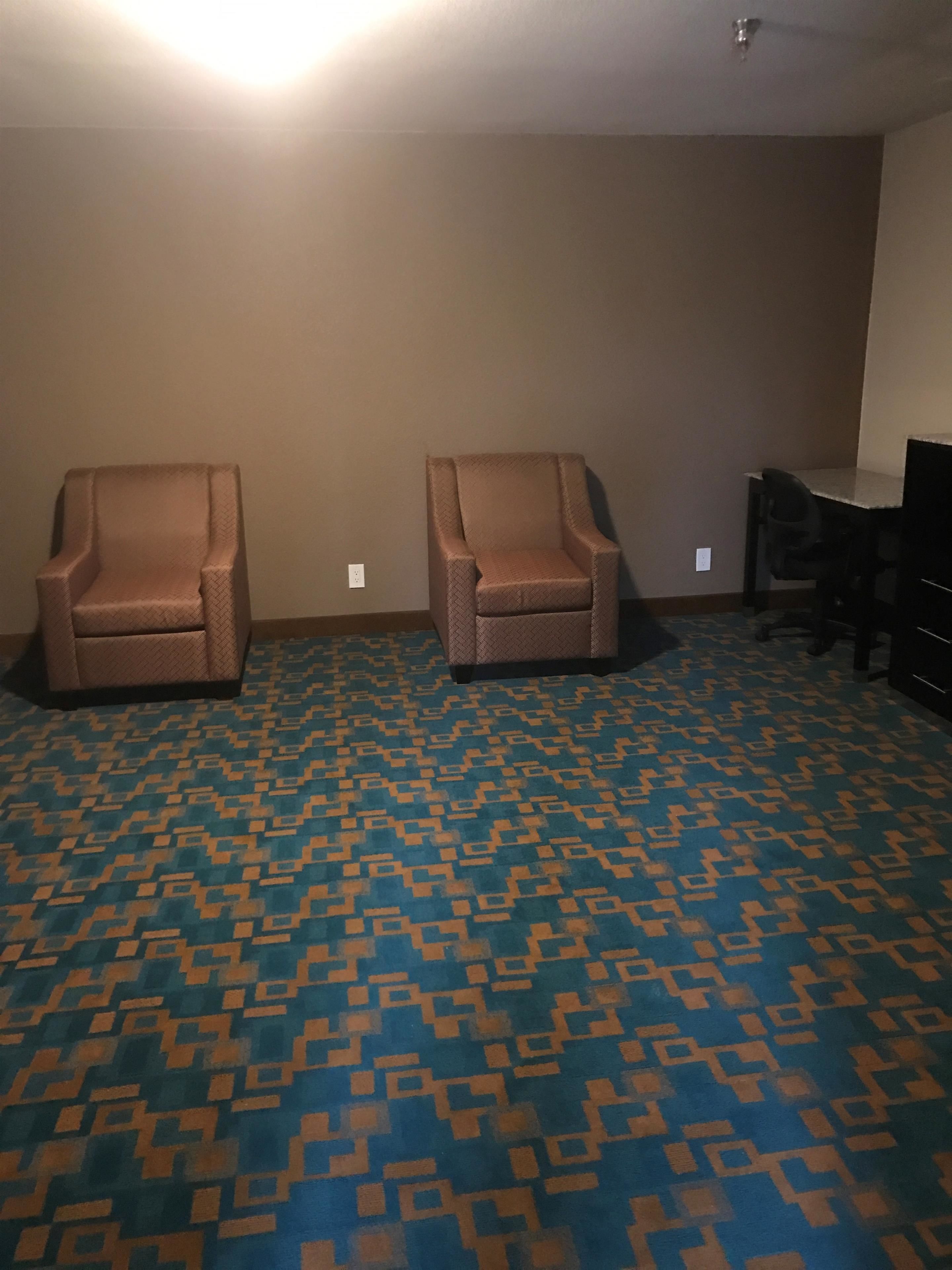 Una habitación con dos sillones, un escritorio y una alfombra estampada.