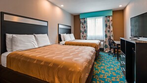 Habitación de hotel con dos camas, un escritorio, una silla y un televisor.