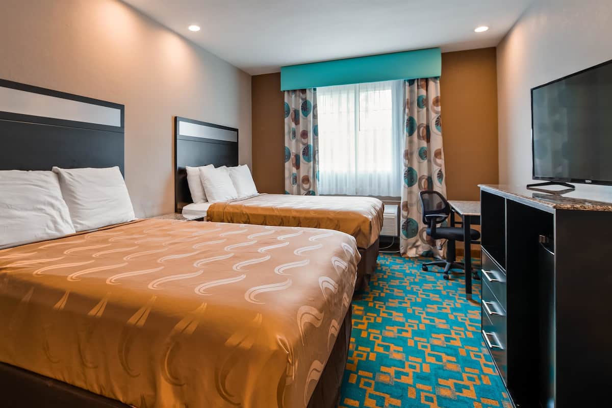 A hotel room with two beds, a desk, a chair, and a TV.