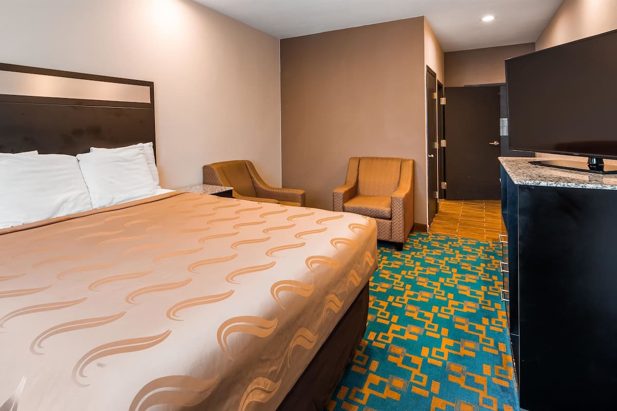 A hotel room with a large bed, a chair, a desk, and a patterned carpet.