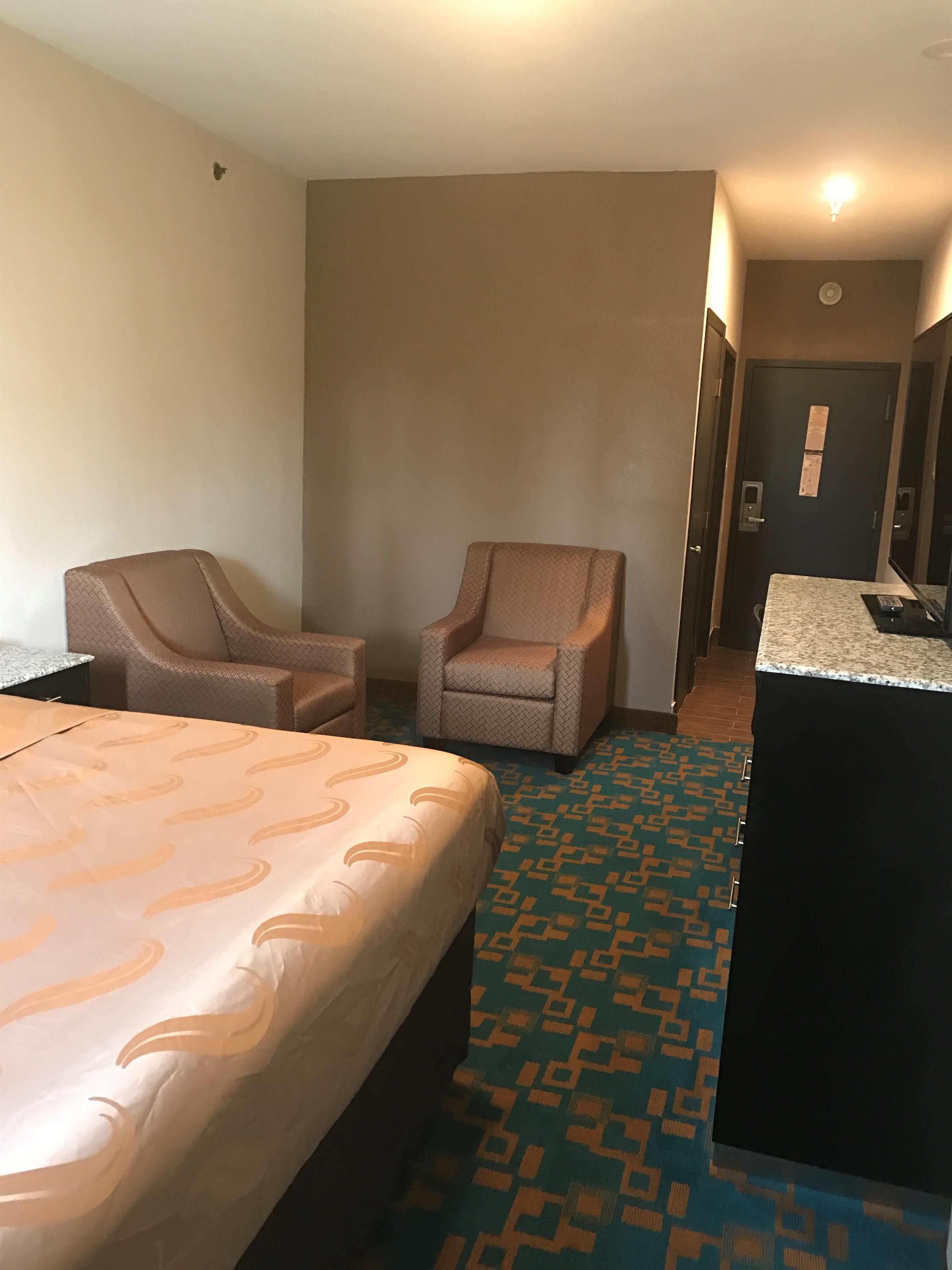 Una habitación de hotel con una cama, dos sillones, un escritorio pequeño y una alfombra estampada.