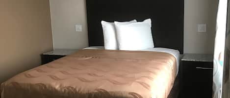 Habitación de hotel con cama, cabecero, mesita de noche y alfombra estampada.