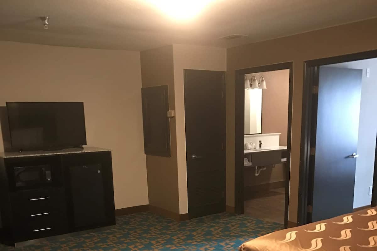 A hotel room with a patterned carpet, a bed, a desk with a television, and a bathroom visible through an open door.