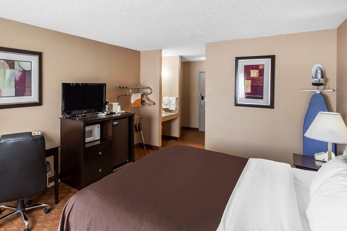 A hotel room with a bed, desk, TV, microwave, and a bathroom visible through an open door.