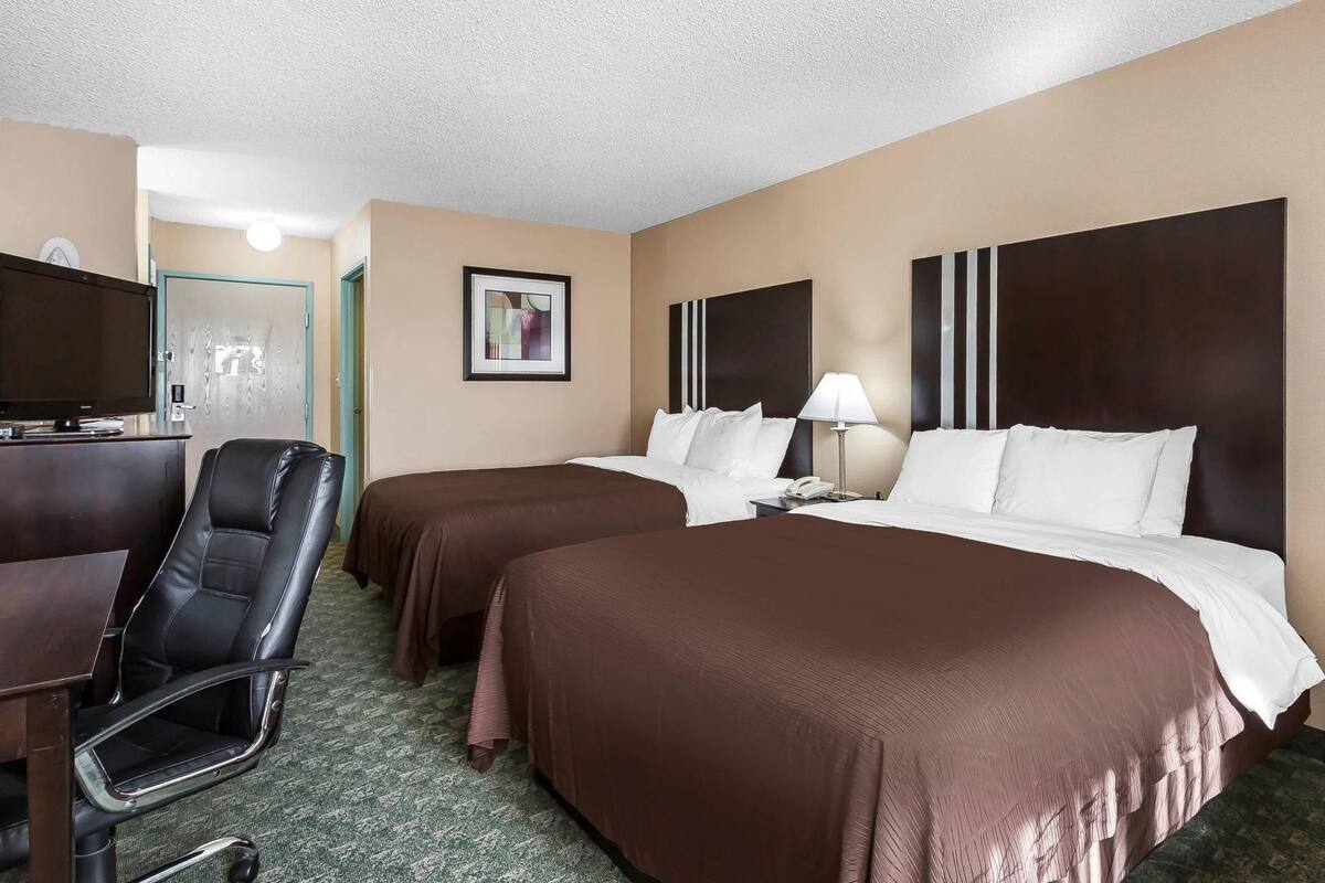 A hotel room with two beds, a desk with a chair, a television, and a framed picture on the wall.