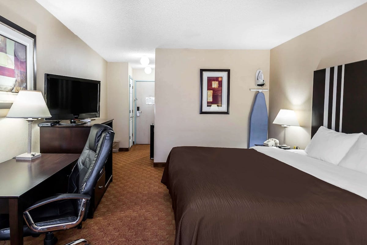 A hotel room with a bed, desk, chair, television, and artwork on the walls.