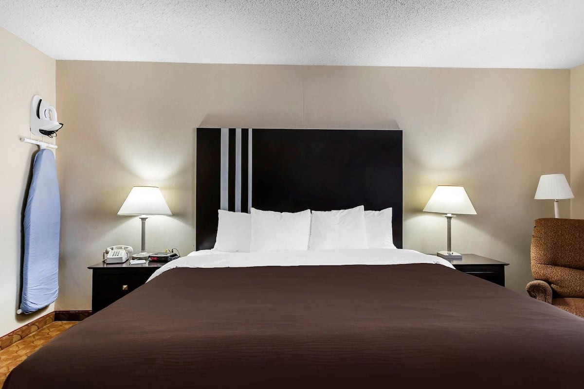 A hotel room with a large bed, two bedside tables, a chair, and a headboard.