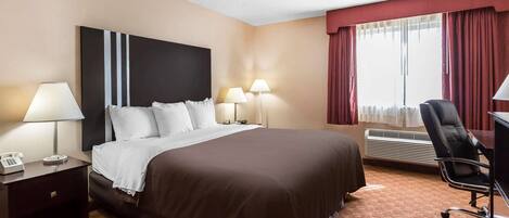 A hotel room with a large bed, two bedside lamps, a desk with a chair, and a window with curtains.