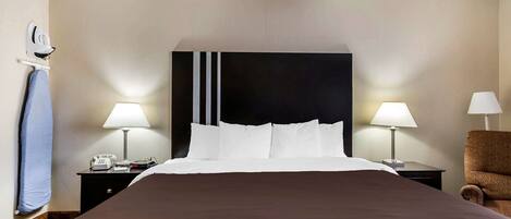 Une chambre d’hôtel avec un grand lit, deux tables de chevet avec des lampes, une chaise et un téléphone fixé au mur.