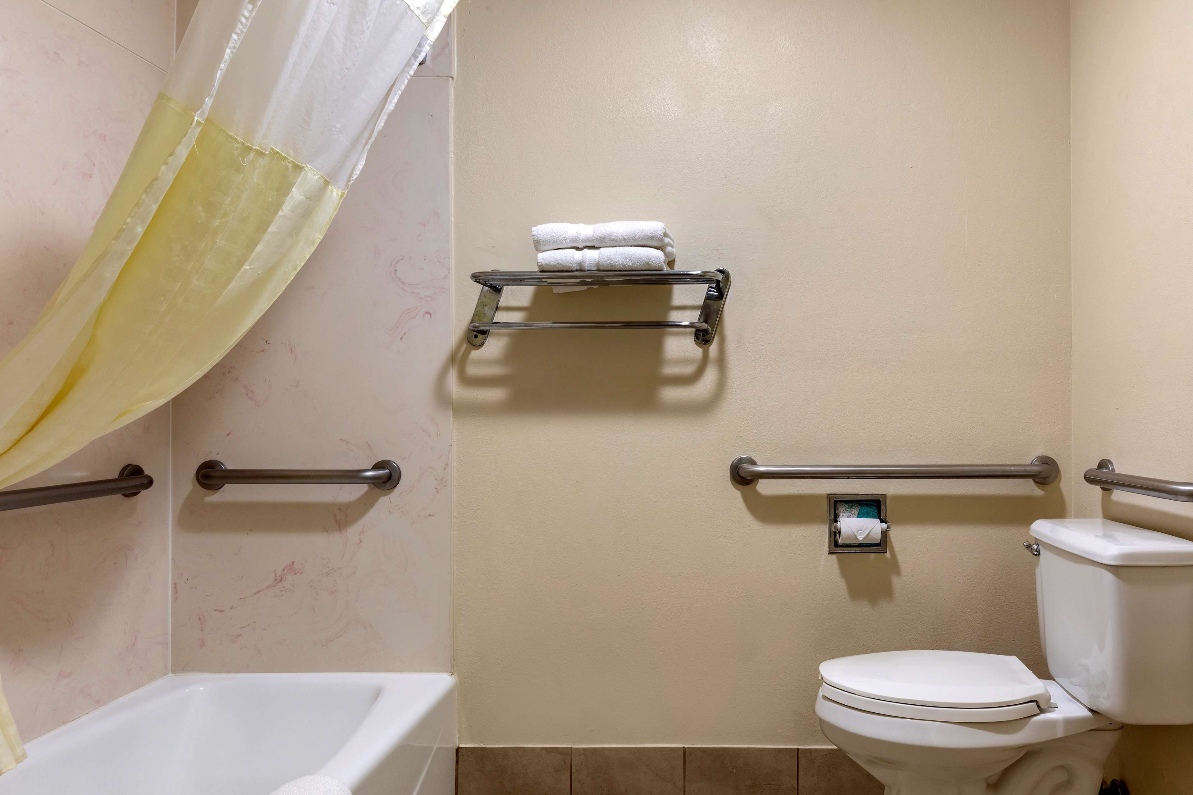 A bathroom with a bathtub, toilet, and handrails.