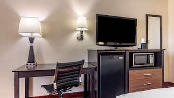 A hotel room with a desk, chair, TV, microwave, refrigerator, and a bed.