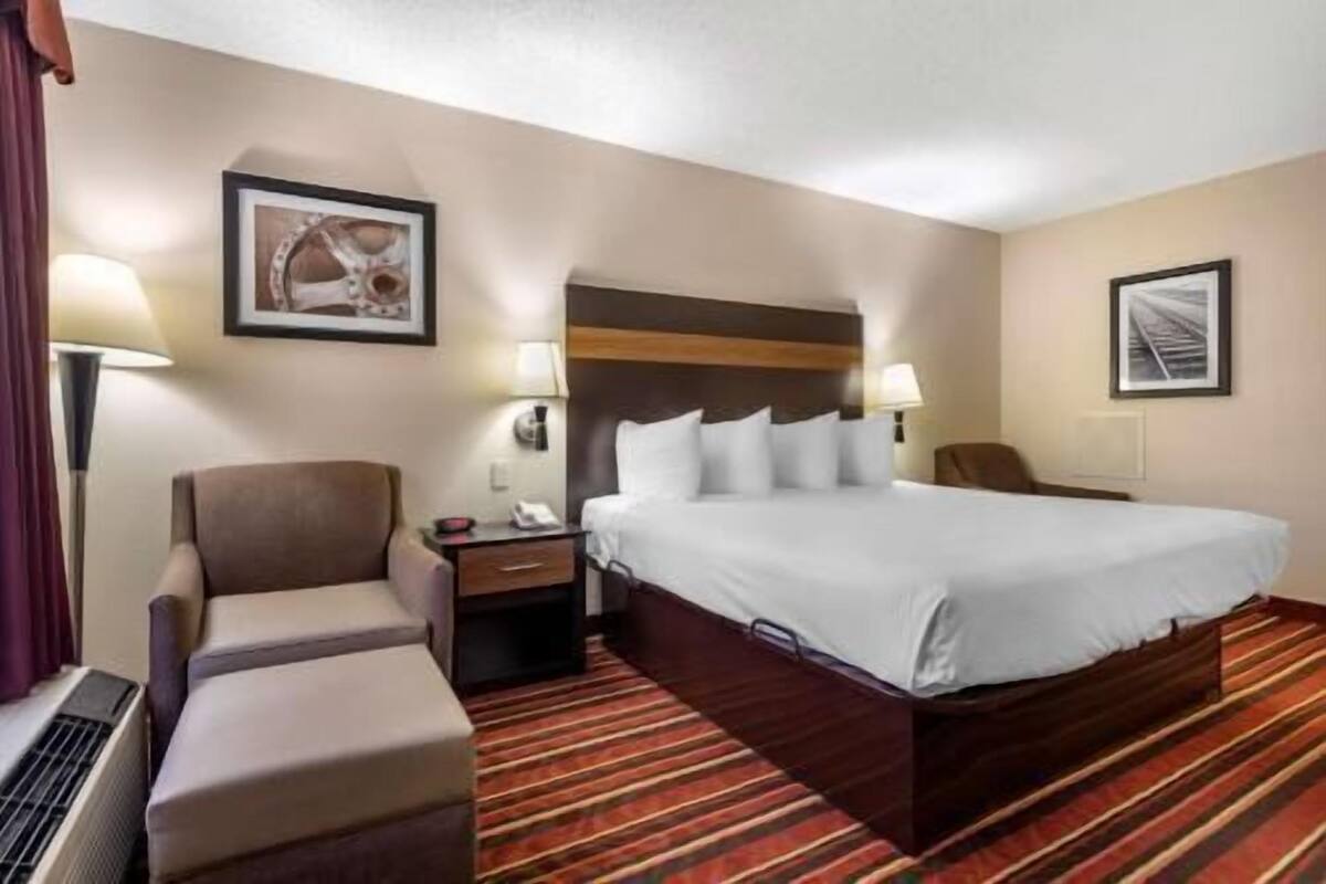 Una habitación de hotel con cama, una silla, una mesita de noche y una lámpara.