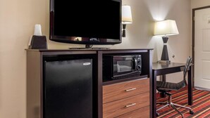 A compact hotel room with a flat-screen TV, a mini-fridge, a microwave, a desk with a chair, and a lamp. - Best Western Lindale Inn (Lindale)