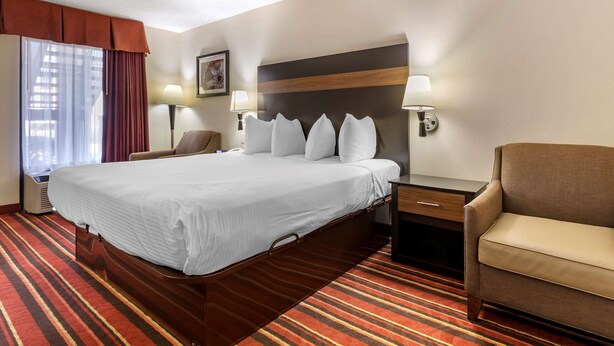 A hotel room with a large bed, two bedside tables with lamps, a chair, and a window with curtains. - Best Western Lindale Inn (Lindale)