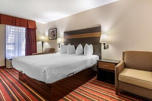 A hotel room with a large bed, two bedside tables with lamps, a chair, and a window with curtains.