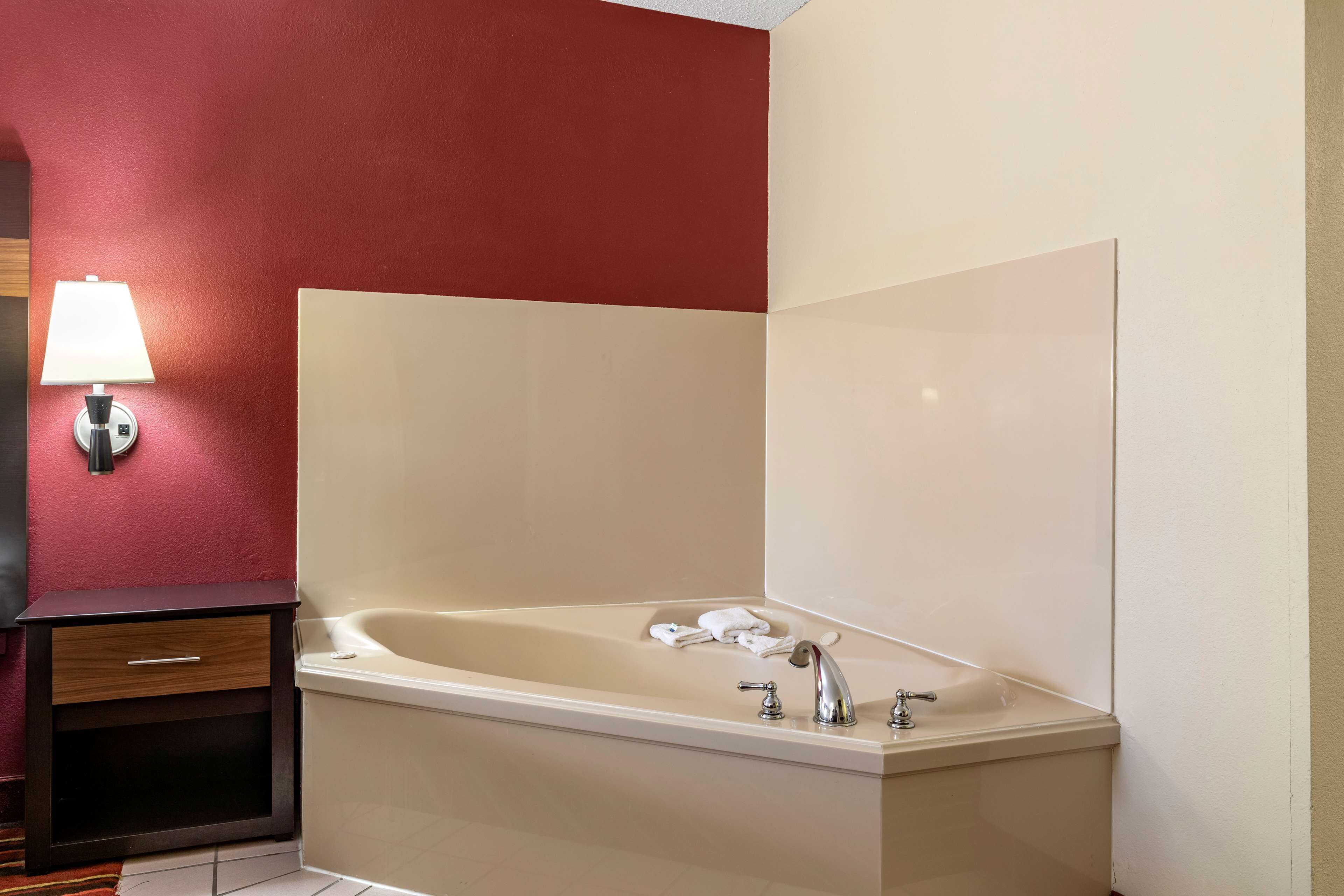 A bathroom with a bathtub, a towel, a lamp, and a wooden cabinet.
