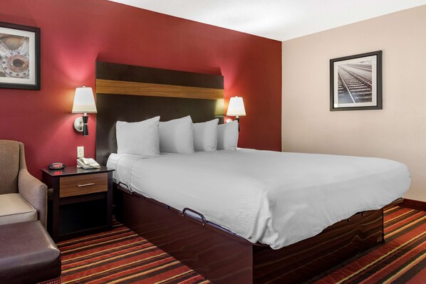 A hotel room with a large bed, two bedside lamps, a nightstand with a phone, a chair, and a striped carpet.