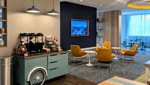 Un moderno vestíbulo de hotel con una estación de café, zona de estar y un amplio ventanal.