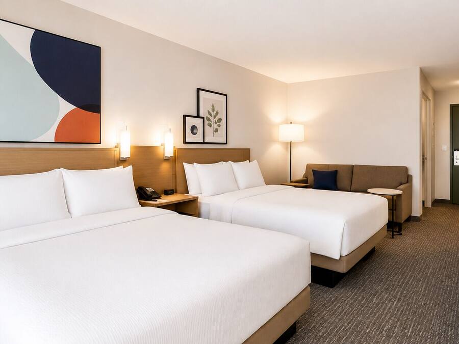 A hotel room with two beds, bedside tables, lamps, a desk, and a door.