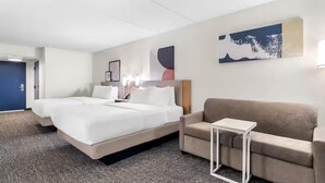 Habitación de hotel con una cama grande, un sofá, una mesita y obras de arte en las paredes.