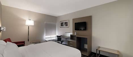 A hotel room with a large bed, a desk with a chair, a television mounted on the wall, and a small bench.