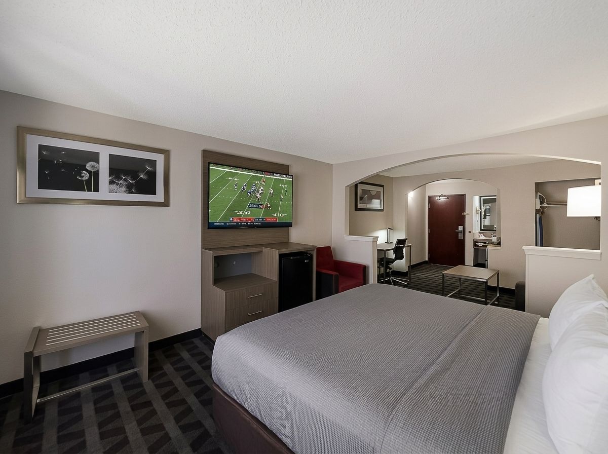 A hotel room with a bed, a desk, a chair, a television, and a small bench.