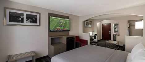 A hotel room with a bed, a desk, a chair, a television, and a small bench.
