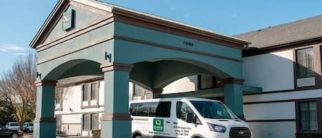A building with a green and white facade, a parked van with a 'Quality' logo, and an American Airlines plane in the background.