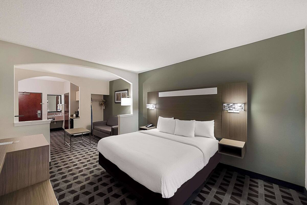 A hotel room with a large bed, a desk, a chair, a nightstand, and a wall-mounted lamp.