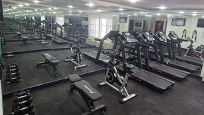 Een fitnessruimte met diverse trainingsapparaten, waaronder loopbanden, hometrainers en krachtapparaten.