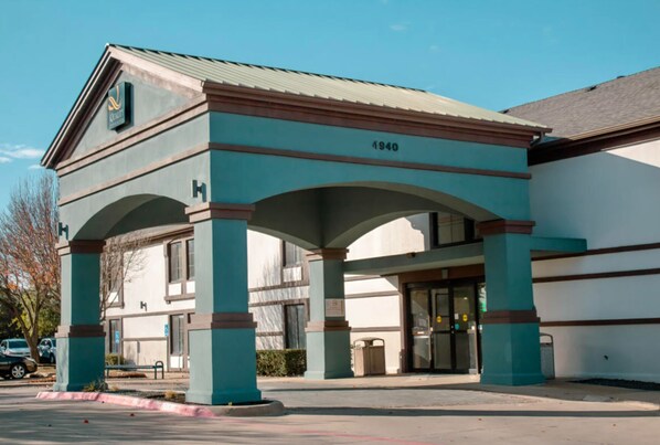 A building with a large entrance, numbered 4940, featuring a covered area with columns and a flat roof. - Quality Inn & Suites Irving DFW Airport South (Irving)