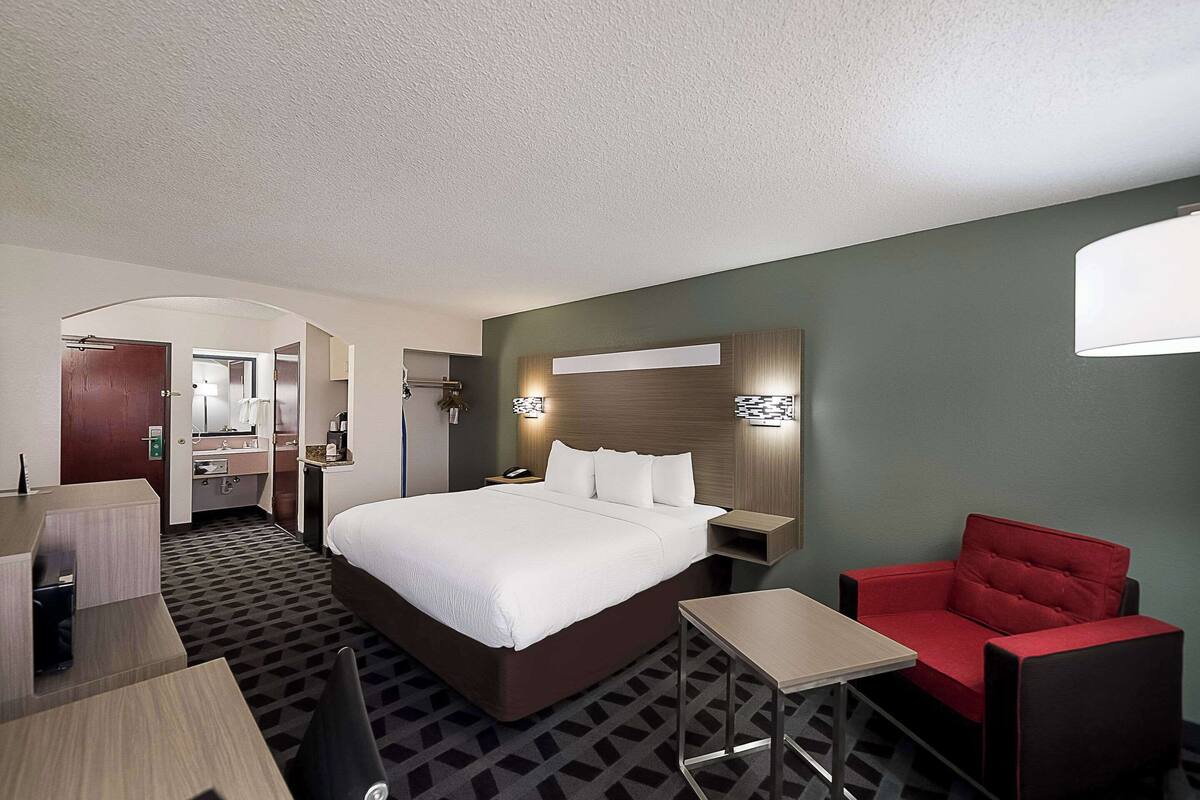 A hotel room with a large bed, a desk, a chair, and a small table.