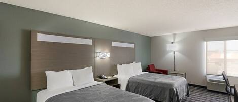 A hotel room with two beds, a desk, a chair, a lamp, and a window.