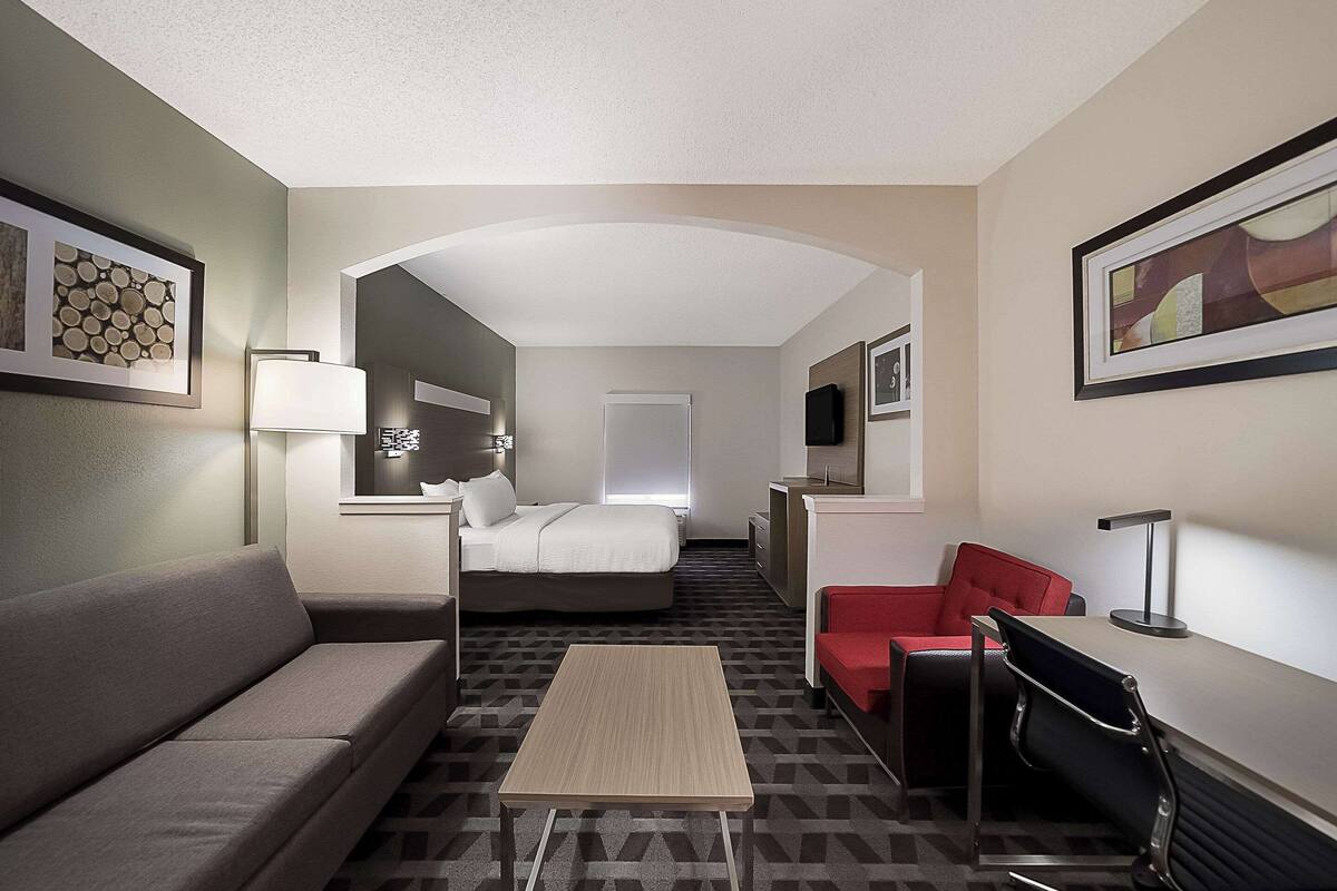 A hotel room with a sofa, a bed, a desk, and a red chair.