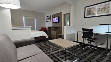 Habitación de hotel con cama, sofá, escritorio con silla, televisor y un cuadro en la pared.