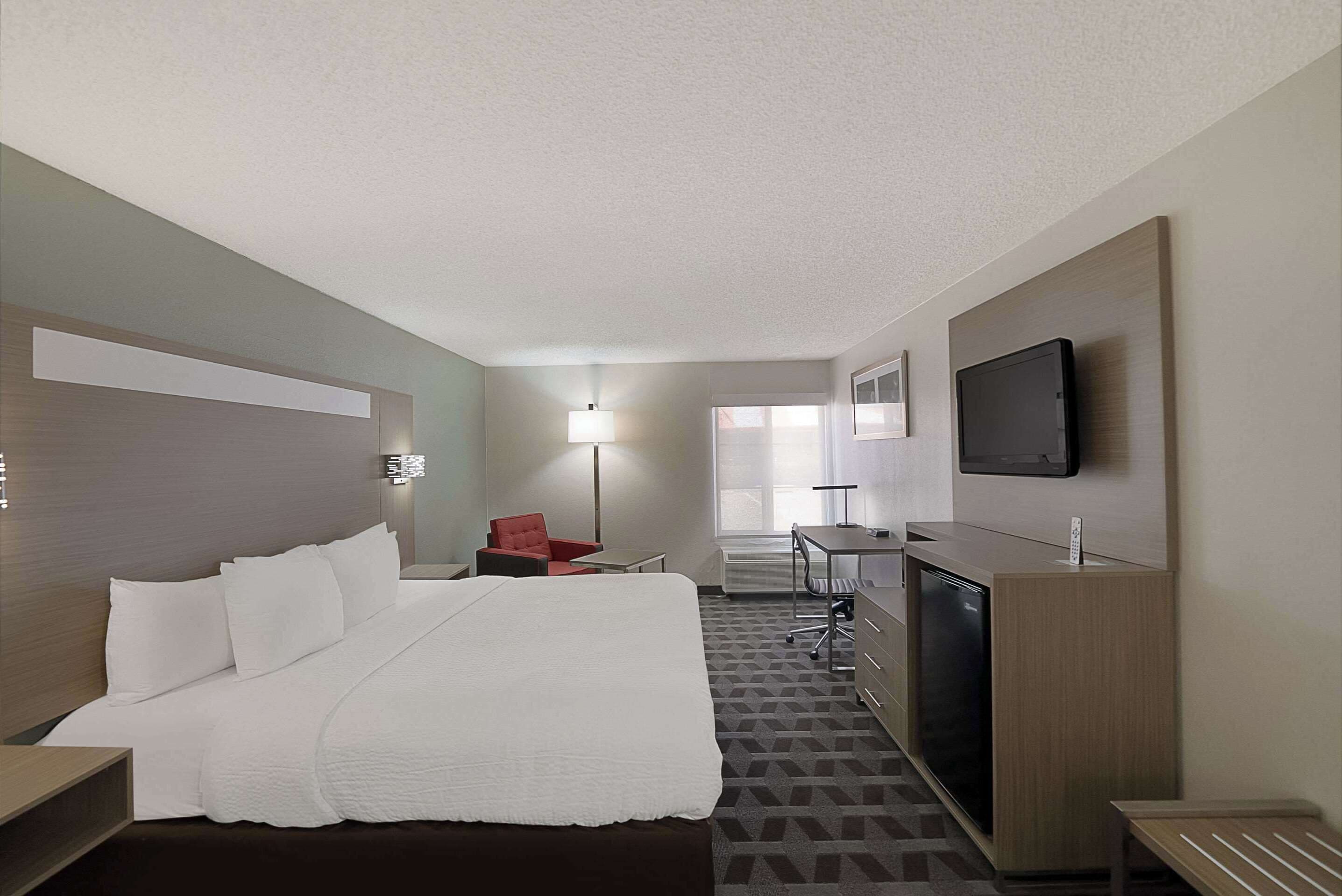 Quarto de hotel com uma cama grande, uma mesa, uma cadeira, uma televisão e um abajur.